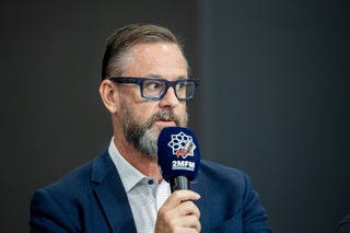 A person with a beard and mustache holding a microphone

AI-generated content may be incorrect.