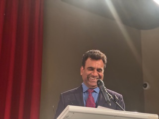 A person in a suit and tie standing at a podium with microphones

AI-generated content may be incorrect.