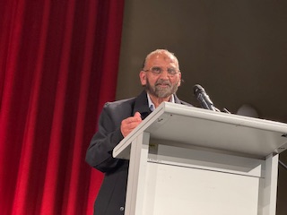 A person standing at a podium with a microphone

AI-generated content may be incorrect.