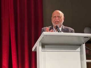 A person standing at a podium with a microphone

AI-generated content may be incorrect.