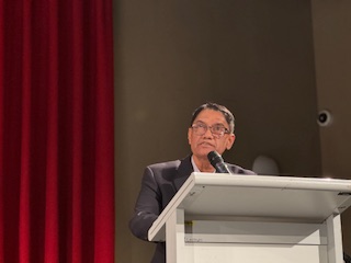 A person standing at a podium with a microphone

AI-generated content may be incorrect.