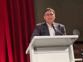 A person standing at a podium with a microphone

AI-generated content may be incorrect.