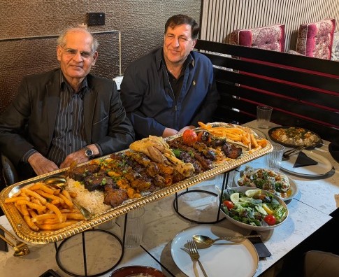 Two men sitting at a table with food on it

AI-generated content may be incorrect.