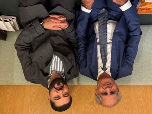 A person in a suit and tie sitting next to another person

AI-generated content may be incorrect.