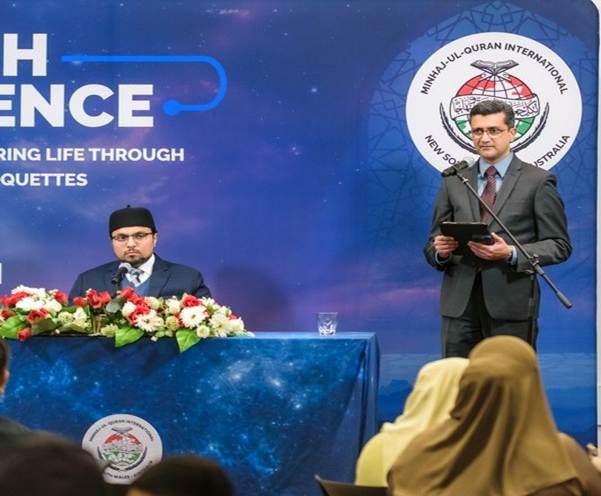 A person standing at a podium with a person in a suit and a black hat

AI-generated content may be incorrect.