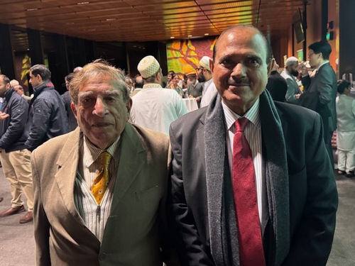 Two men standing together in a room with many people

AI-generated content may be incorrect.