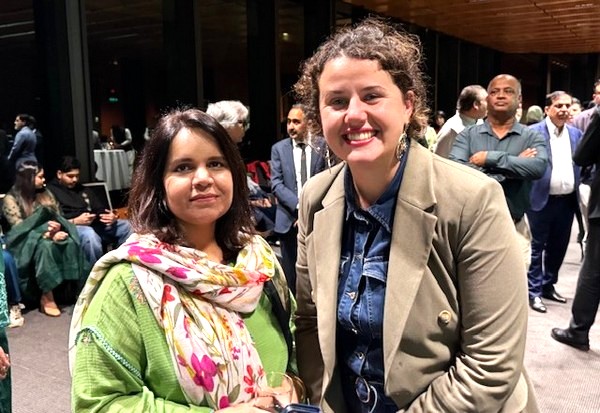 Two women standing together in a room with people around them

AI-generated content may be incorrect.